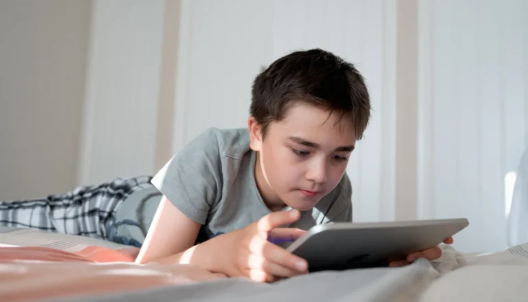 Un enfant concentré allongé sur un lit, utilisant une tablette pour jeux ou apprentissage en ligne à la maison.
