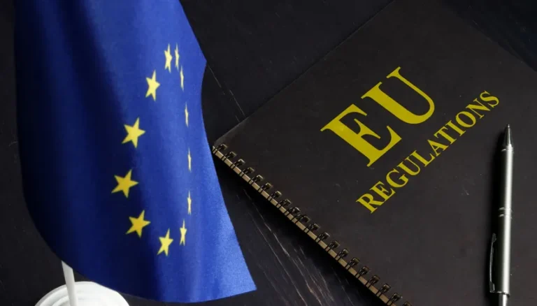 Drapeau de l'Union européenne à côté d'un cahier intitulé "EU REGULATIONS" et d'un stylo, illustrant la réglementation juridique de l'intelligence artificielle en Europe.