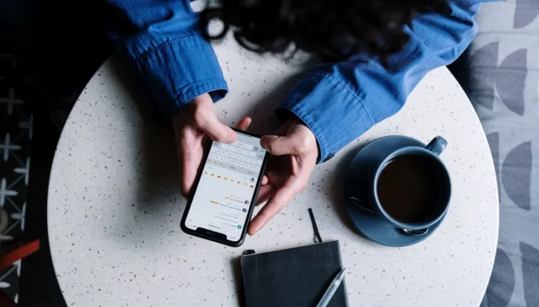 Personne utilisant un smartphone pour vérifier des messages, avec une tasse de café et un carnet sur une table, illustrant la régulation du chiffrement face à la désinformation.