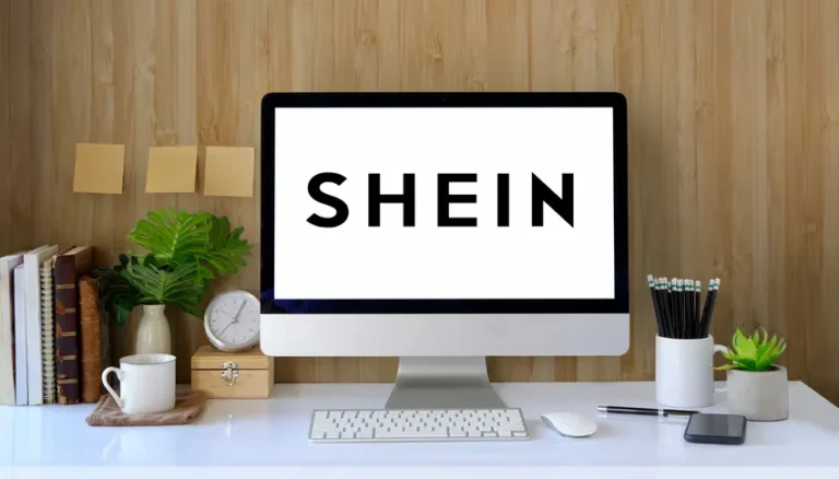 Espace de travail moderne avec un ordinateur affichant le logo SHEIN, entouré de plantes, livres, et accessoires de bureau, dans un environnement professionnel et épuré.