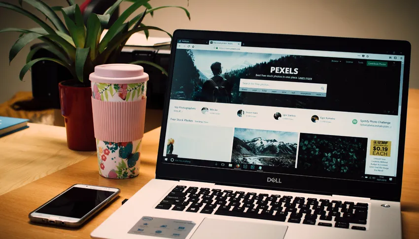 Espace de travail avec un ordinateur portable affichant le site Pexels, une tasse à café décorée, un smartphone, et des plantes vertes pour un environnement professionnel moderne.