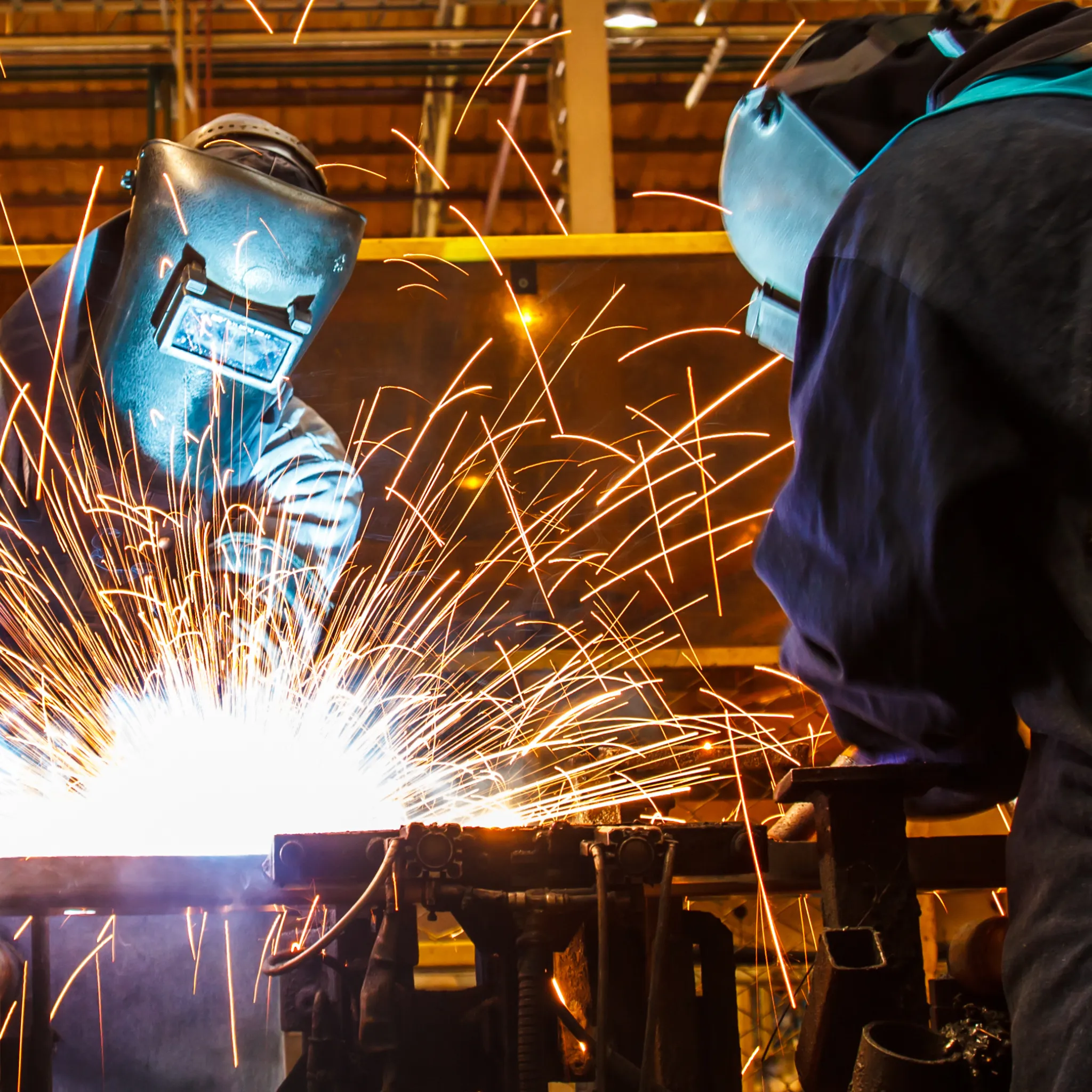 Deux soudeurs en protection effectuant une soudure avec étincelles dans un atelier industriel.
