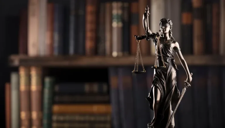 Statue de la justice avec balance et épée, symboles du droit, dans une bibliothèque de livres juridiques.